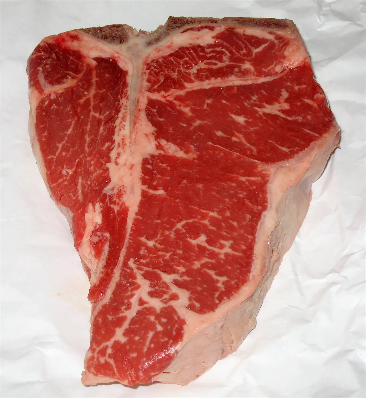 Raw well-marbled T-bone steak showing the strip and tenderloin on a cutting board