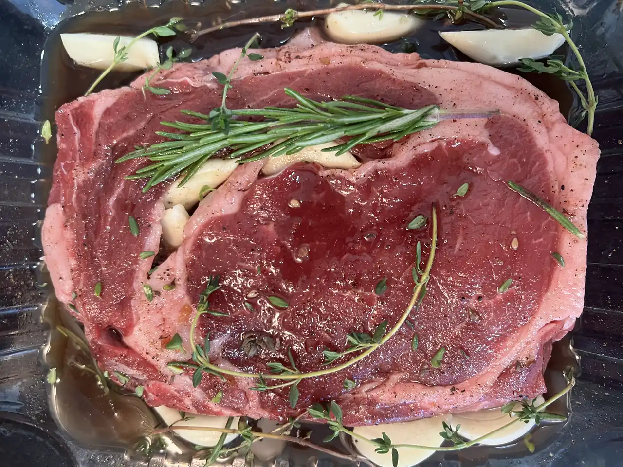 Raw ribeye steaks with garlic and fresh herbs before cooking